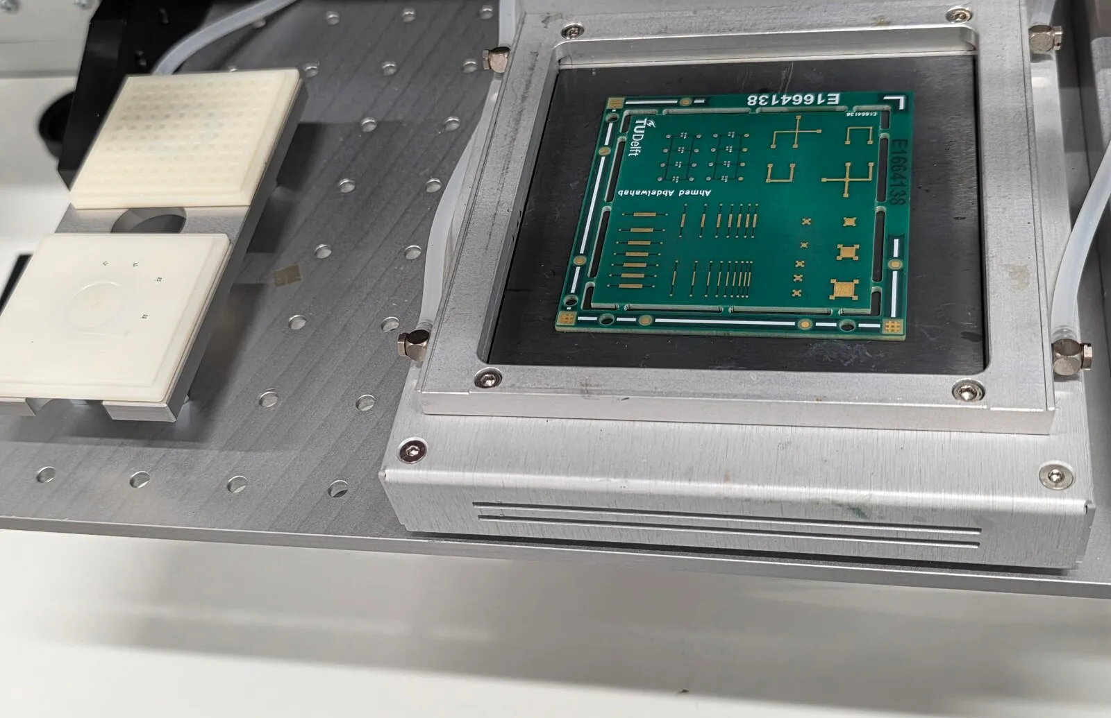 Characterization board clamped on the vacuum chuck of a die bonder, with two white die trays on the stage beside it
