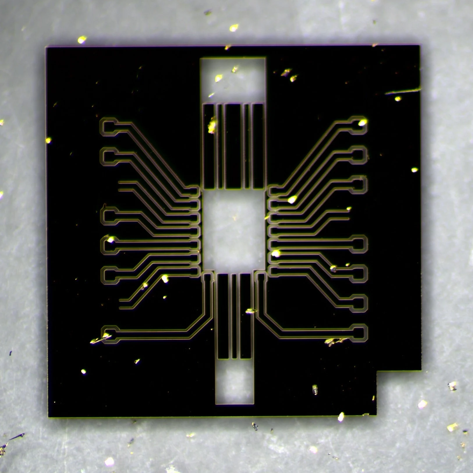 Dark-field micrograph of the fabricated interposer before bonding: black metal with thin bright outlines tracing the same pattern as the layout, and an open window in the centre