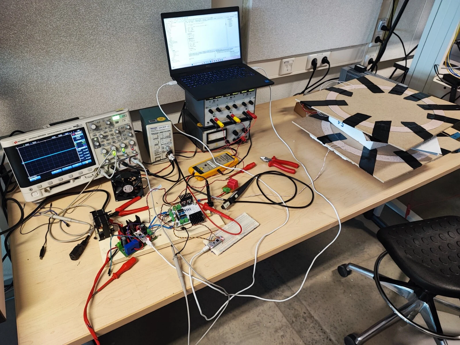 Lab bench with an oscilloscope, power supplies, a laptop, the converter boards wired up, and the two coils stacked on boards to the right
