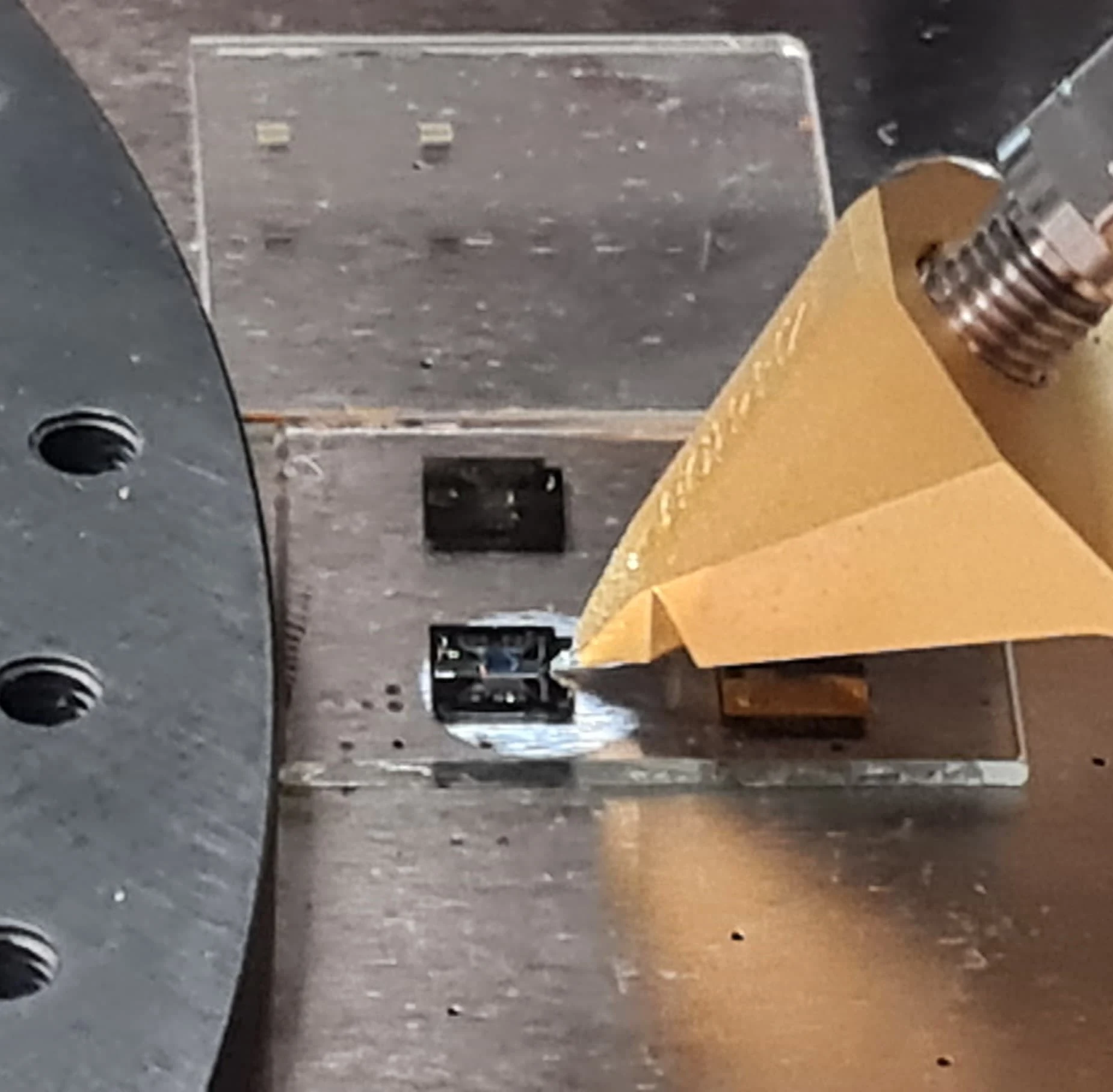 Photograph of a gold-coloured GSG RF probe landing on a small bonded die on a glass slide on the probe-station chuck
