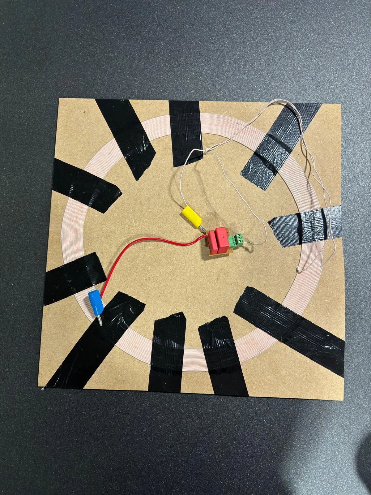 A flat spiral coil of Litz wire taped to an MDF board, with a small board of capacitors and a terminal block in the centre