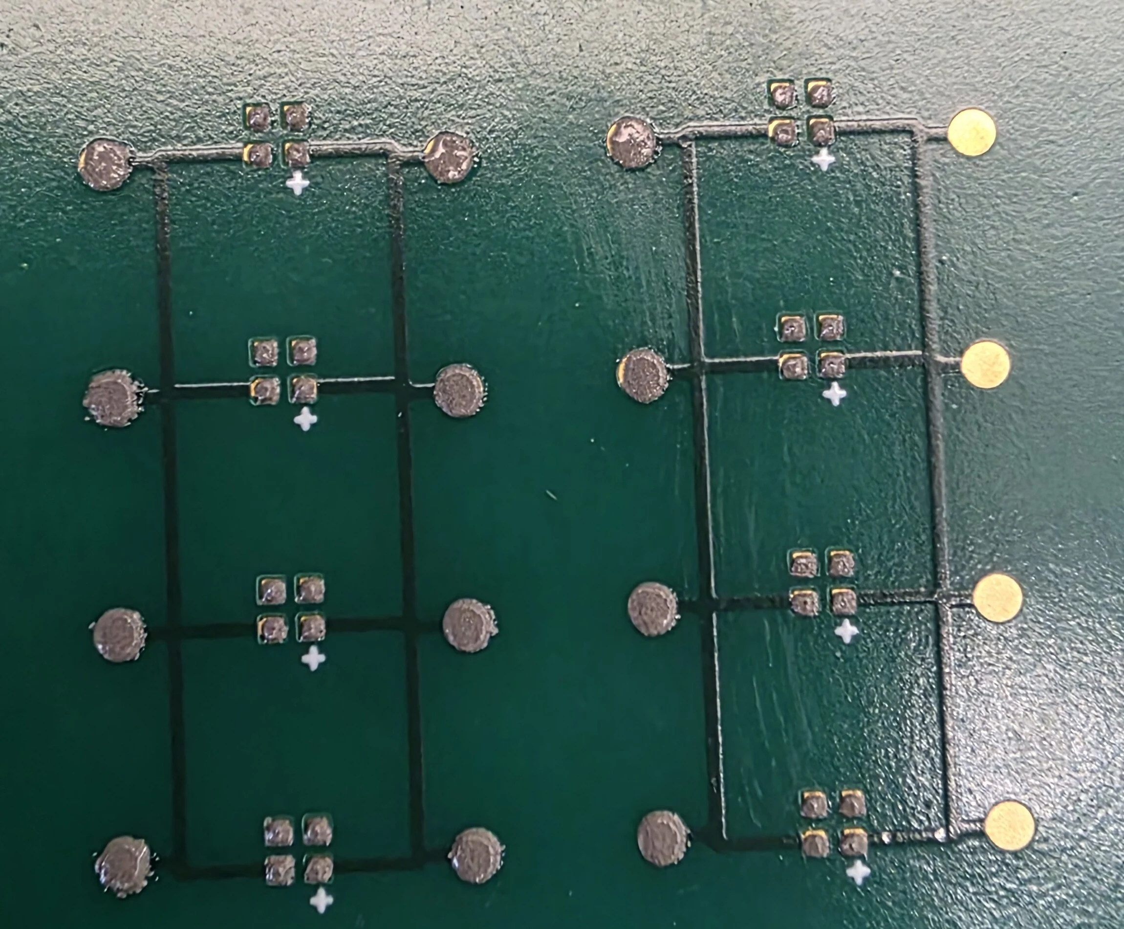 Close-up of solder paste deposits on the four-pad LED sites and round contact pads of a green test board, with some pads still bare gold