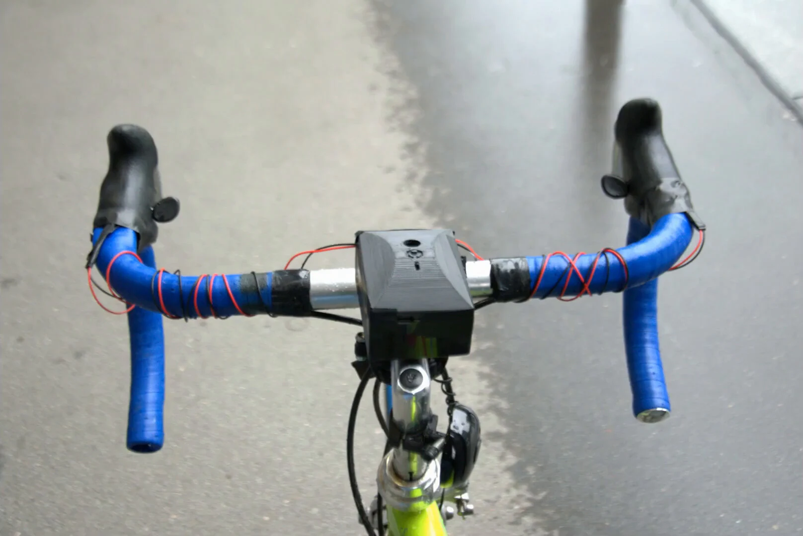 The black 3D-printed Pulse unit on the stem of a road bike with blue bar tape, red and black motor wires wound along the bars to a vibration motor at each grip