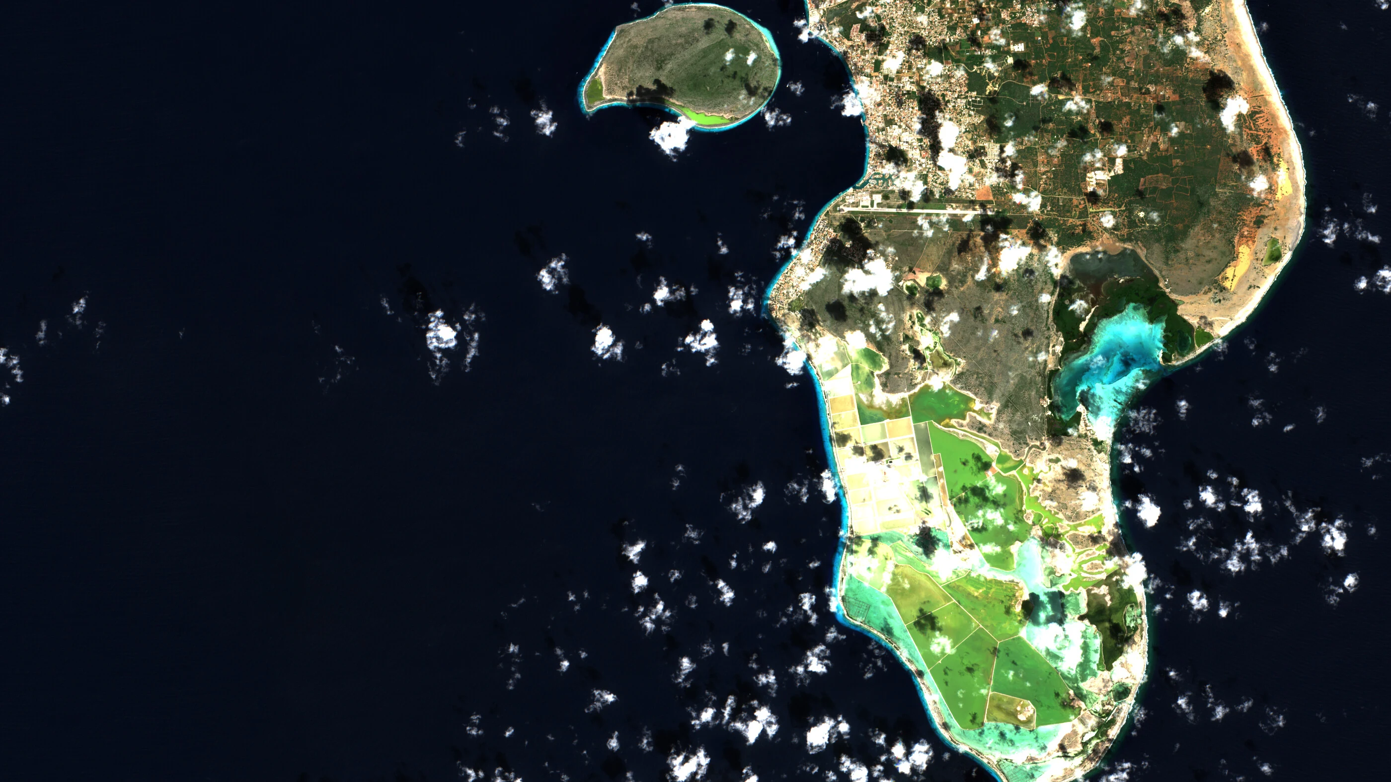 Sentinel-2 true-colour view of south Bonaire and Klein Bonaire: dark ocean, scattered small clouds, salt pans in the south and the cyan shallows of Lac Bay on the east coast