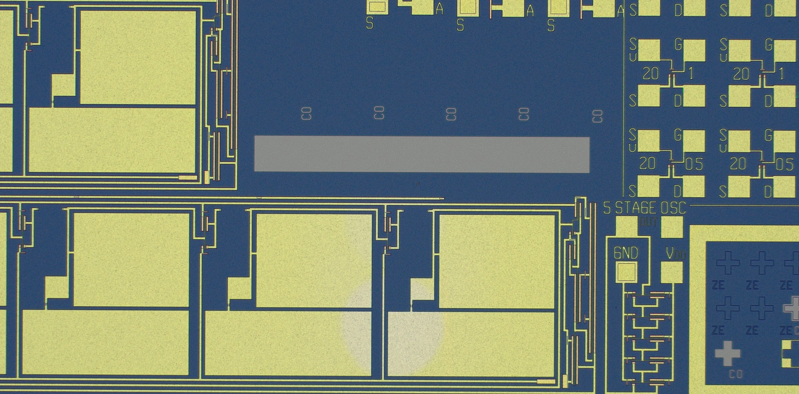 Optical micrograph of a BICMOS5 die after wet etching: gold aluminium pads and interconnect on blue field oxide, with transistor test pads labelled S, G, D and a block labelled 5 STAGE OSC